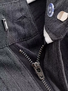 Detail of dark grey trousers showing the zipper, button, and twill fabric texture