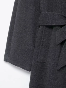 Detailed close-up of dark grey wool coat featuring tied waist belt and fabric texture
