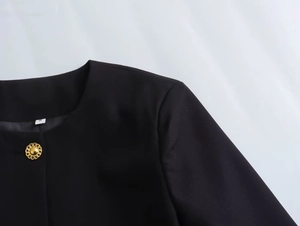 Detail of round neck black jacket featuring an embossed gold button and fabric texture