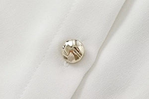 Macro shot of a twisted gold metal button on a white textured crepe fabric shirt