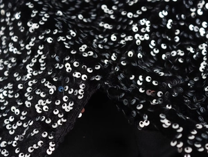 Macro shot of shimmering silver sequins stitched on black asymmetric evening dress fabric