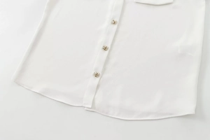 High-quality detail of a white crepe blouse hem showing three ornate gold buttons.