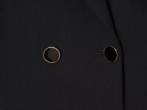 Detailed close-up of textured black blazer fabric with premium gold-rimmed buttons