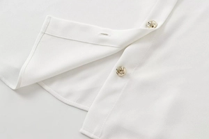 Detail of white crepe blouse with gold embossed buttons and premium woven texture
