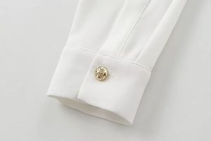Close-up of white long sleeve cuff featuring a textured gold metal button detail