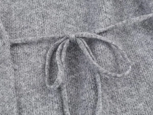 Detailed close-up of grey knitted wool fabric with a delicate waist tie string
