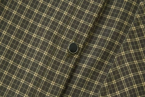 Macro detail of dark green plaid shirt showing fabric texture and silver-rimmed black button