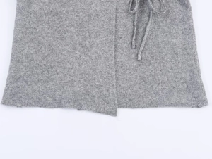 Detail of grey knitted coat showing side tie-up strings and asymmetric hemline design