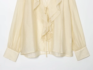 Detail of ruffle V-neckline with delicate ties on cream chiffon blouse for women