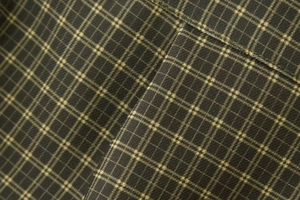 Macro shot of dark green plaid fabric texture with fine yellow check and sewing detail