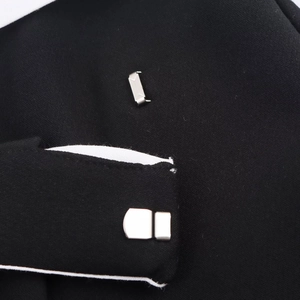 Detail of silver metal fastener on black fabric skort with contrast white piping