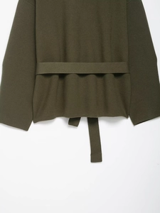 Detail of olive green knitted jacket featuring textured fabric and matching waist belt