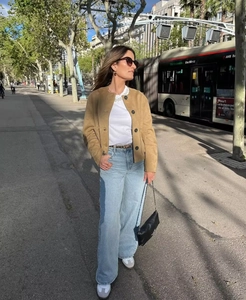 Outdoor street view of a woman wearing a chic camel suede bomber jacket and wide-leg jeans