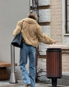 Street style view of a beige faux fur jacket paired with blue jeans and a black tote bag