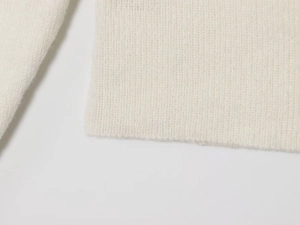 Gros plan sur la maille blanche du pull montrant les poignets côtelés et le tissu doux