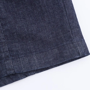 Détail de robe en jean ajustée montrant le sergé bleu foncé et l'ourlet à double couture