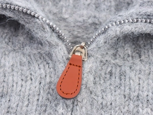 Close-up of silver metal zipper with brown leather pull on grey knit sweater fabric