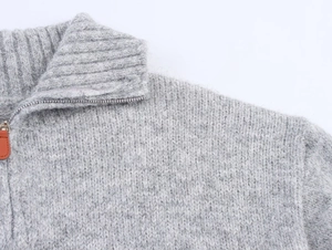 Close-up of grey chunky knit sweater featuring half-zip collar and leather puller