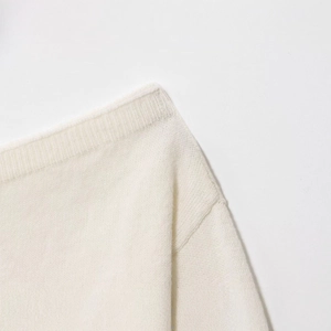 Gros plan sur un pull en maille ivoire à épaules dénudées montrant la texture côtelée douce
