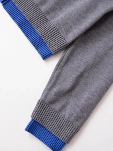 Detail of grey knit fabric with blue ribbed cuff stitching on a long sleeve cardigan