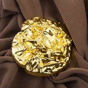 Detail of golden irregular hammered metal brooch on pleated fabric texture