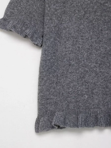 Dettaglio di un maglione grigio a maglia con bordi a volant e texture in lana