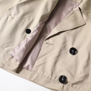 Detail of khaki cropped trench coat with double-breasted buttons and twill fabric texture