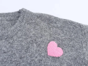 Dettaglio maglione grigio in maglia con applicazione a cuore rosa e consistenza morbida