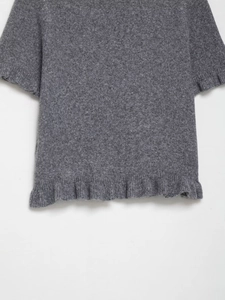 Dettaglio del maglione grigio a maniche corte in maglia con bordo a balze e trama di lana