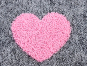Dettaglio di una toppa a cuore rosa pelosa su maglia grigia per maglioni donna