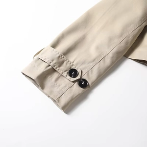 Detailed close-up of khaki trench coat cuffs with dual black buttons and twill fabric texture