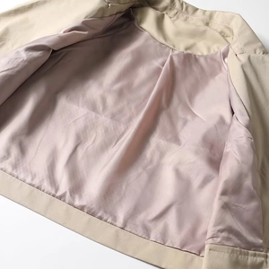 Detailed close-up of beige trench coat fabric with soft lavender satin inner lining texture