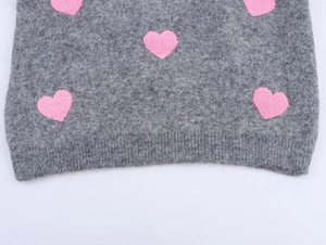 Dettaglio maglione grigio peluche con motivi a cuore rosa e orlo a costine rifinito