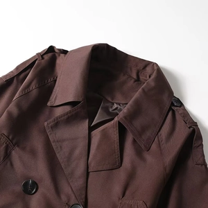 Detailed close-up of dark brown trench coat featuring notch lapels and epaulette buttons