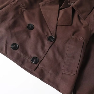 Detail of dark brown double-breasted cropped jacket with resin buttons and twill texture