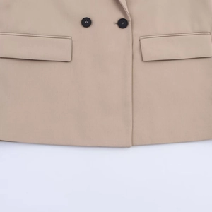 Detailed view of beige double-breasted blazer with black buttons and flap pockets
