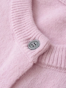 Detailed macro view of pink knit wool cardigan featuring ribbed neck and grey button