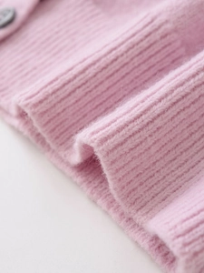 Detail of pink knit sweater showing ribbed cuffs, wool blend texture, and grey button