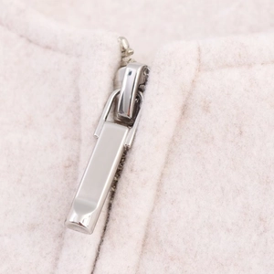 Close-up of polished silver metal zipper detail on soft cream pilot bomber jacket