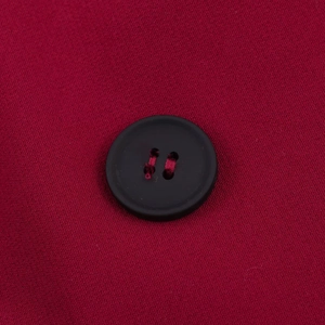 Macro detail of a black four-hole button on red plain weave fabric blazer