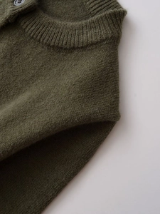 Detail of dark olive wool knit cardigan featuring ribbed crew neck and shoulder button