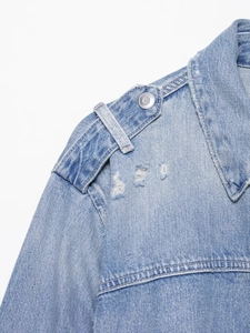 Détail d'une veste en jean bleu clair avec épaulettes, bouton en métal et effets déchirés