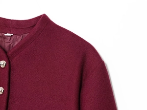 Detail of burgundy wool blend coat featuring silver round metal buttons and collarless neck
