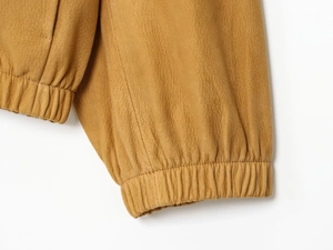 Detail of camel leather aviator jacket featuring premium texture and elastic ribbed cuff
