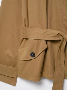 Close-up of khaki trench coat featuring waist belt, pocket flap and black button detail