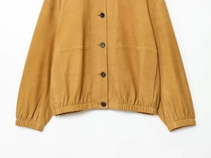Detail of mustard yellow leather bomber jacket featuring button closure and elastic hem
