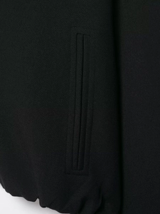 Détail d'une veste noire avec poche passepoilée verticale et ourlet élastique froncé