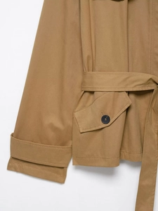 Detail of khaki trench coat featuring cuff straps, waist belt, and buttoned flap pockets