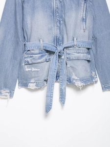 Détail d'une veste en jean bleu clair avec taille ceinturée et bords usés et déchirés