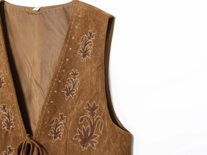 Gros plan du gilet en daim marron vintage avec broderies florales et lacets au cou